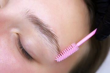 combing the eyebrow hairs after the eyebrow lamination procedure with a pink brush