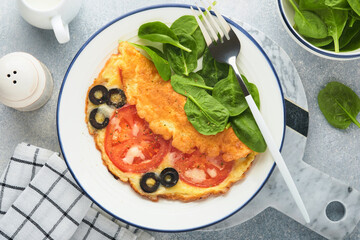 Omelette with tomatoes, black olives, cottage cheese and green spinach herbs on white plate on grey concrete background. Delicious breakfast. Healthy breakfast food. Top view.