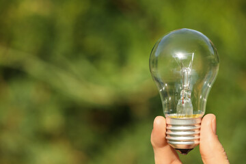 Woman holding incandescent light bulb on blurred green background, closeup. Space for text