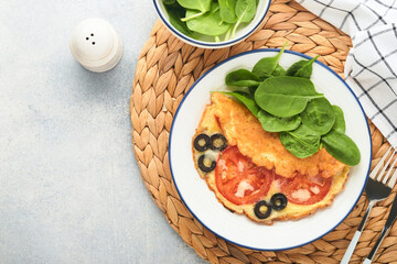 Omelette with tomatoes, black olives, cottage cheese and green spinach herbs on white plate on grey concrete background. Delicious breakfast. Healthy breakfast food. Top view.