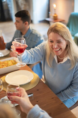 Cheerful mid adult woman raising wine glass at dinner party. Family having meal at home together. Family party concept
