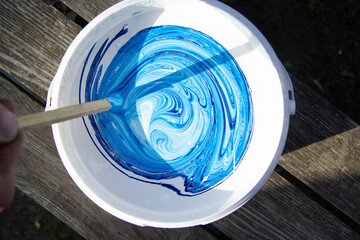 blue and white paint is stirred in a bucket