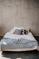 Fototapeta na wymiar bed with white and grey linens against the background of the wall. minimalistic interior in loft style. goods and textiles for the bedroom. interior designer services.