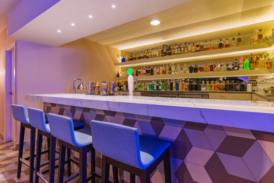 Modern bar counter with stools and different bottles of alcohol - Powered by Adobe