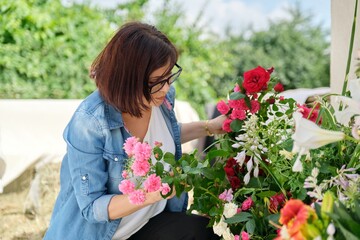 Fototapeta premium Woman florist making flower arrangement in basket outdoor.