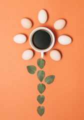 Creative concept made with cup of coffee, green leaves and eggs on pastel brown orange background. Minimal flat lay mockup.