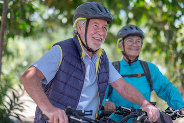 Active senior couple with electrobikes standing outdoors in the park. Two happy elderly people running in nature with their bicycles enjoying healthy lifestyle