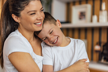 Obraz premium Close up of a smiling adult mother and her son in a hug, at home.