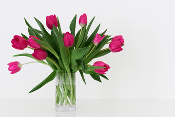 Tulip flowers in a transparent small vase standing on white table. Bouquet of spring flowers