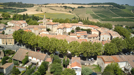 Aerial shot of a medieval round village with red tile roofs surrounded by green fields and trees