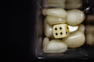 Top view of a white dice and white plastic stones in a glass bottle with black background