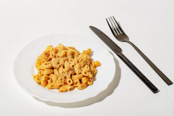 Curly Italian pasta with sauce on a white plate. Minimalism. White background. Pasta in cheese sauce. Knife and fork are black.