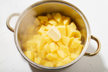 Boiled potatoes in a pot. Hot potato cubes with a piece of butter. Cooking boiled potatoes, mashed potatoes. Steam is coming. White background.