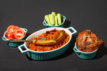 Jollof rice with fried banana, baked chicken. Rice with tomatoes, onions, spices. Traditional national Nigerian food. Dark background.