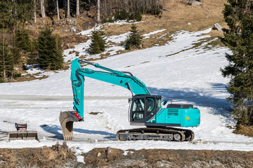 turquoise excavator in snowy landscape constructing a torrent control in the mountains