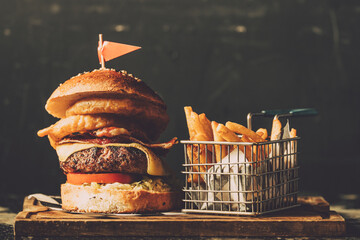 A delicious cheese burger  with onion rings and fries served on a table wood
