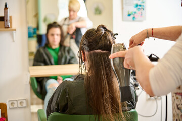 A woman in a hairdresser salon and the barber hairdressing her hair with comb and hairdryer