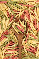 Fusilli pulgiesi tri colored pasta in an olive wood spoon and forming an abstract background. Healthy Italian carbohydrate food concept.