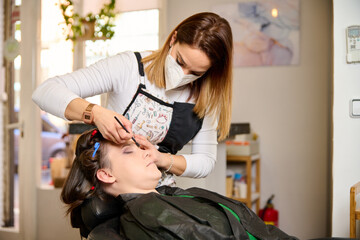 Woman in a hairdresser salon with her hairdressing and makeup artist putting some makeup on her eye