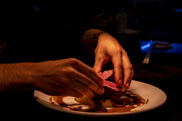 Close-up shot of the chef placing steak sliced in half with mashed potatoes in dim lighting.