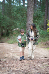 Boy and wo with cameras walking in forest. Dark-haired mother and son in coats getting ready to take pictures. Parenting, family, leisure concept