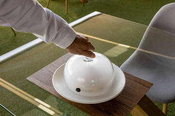 Angle shot of a chef opening a glass dome of a dish. © Damián Méndez/Wirestock Creators