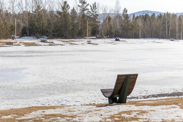 Empty wooden chair-bench for solitude on the snow-covered shore of a winter lake. Walk in the park...