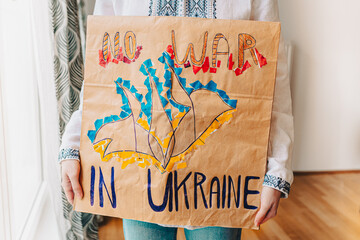 teenage girl in an ethnic white embroidered shirt, with banner in her hands, inscription No war in Ukraine, Children against aggression of Russia, with request to protect Ukrainian people and freedom