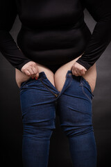 fat woman pulling jeans on herself on a black background