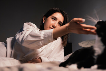 Woman playing with a cat lying on the bed