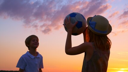 Brother and sister play ball, throw the ball into each other's hands. Teenagers girl and boy have fun playing in the backyard in the rays of the setting sun. Children's dreams