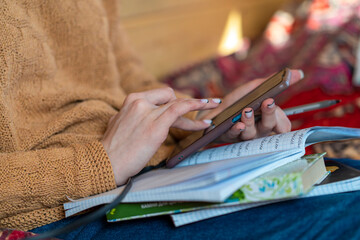 Close up of a woman's hand holding a mobile smartphone and using a pen while making notes in a notebook. Student studying online, reading e-book, online learning.