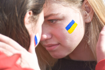 Portrait of two girls looking at each other  with flags of Russia and Ukraine on cheeks. Stop war...