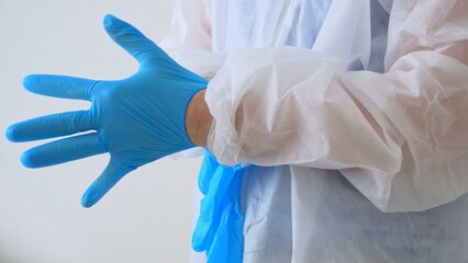 Close-up of putting on surgical gloves. A medical worker in a disposable washing gown puts on blue latex gloves to work in an infected area or before a surgical intervention. Caronovirus.
