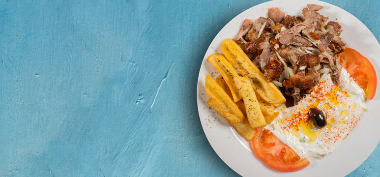 Greek dish of Gyro with lamb meat with onion accompanied by French fries and Tzaziki sauce with tomato on banner format