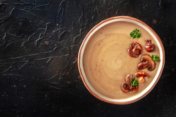 Mushroom soup in a rustic bowl, overhead shot on a black slate background with copy space