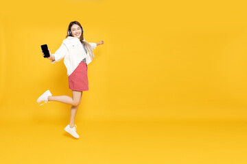 Young Asian woman listening favourite music on mobile phone application with wireless headphones and dancing isolated on yellow background, Full body composition