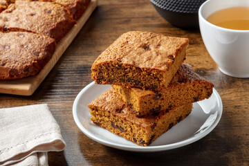 Blondie brownie dessert bars with chocolate chips, on a dark rustic wooden table with tea