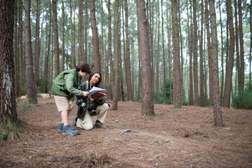 Naklejka na ściany i meble Merry boy and woman with cameras walking in forest. Dark-haired mother and son in coats getting ready to take pictures, discussing route. Parenting, family, leisure concept