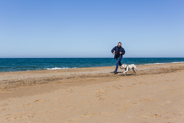 A man with a Labrador dog runs along the beach in the cold season