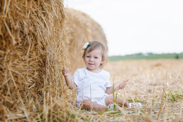 Naklejka na ściany i meble little girl playing in haystacks. Having fun away from city on field full of golden hay.