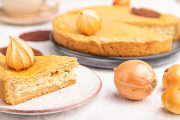 Autumn onion pie decorated with leaves and cup of coffee on gray concrete background. Side view, selective focus.