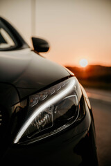 Vertical shot of the front part of a black luxury car at sunset © Tarik Pajić/Wirestock Creators
