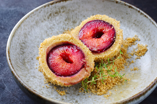 Traditional Austrian plum dumpling with a backed prune in a dough coat and butter crumbles served as close-up in a Nordic design bowl