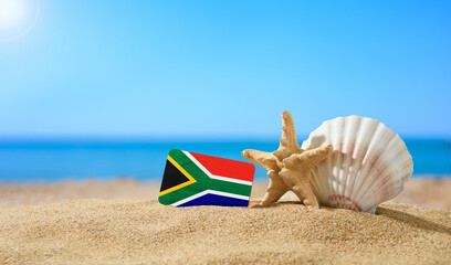 Tropical beach with seashells and South Africa flag. The concept of a paradise vacation on the beaches of South Africa.