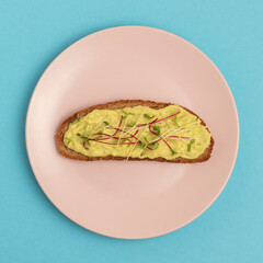 A slice of bread smeared with avocado mash and seasoned with microgreens. Avocado sandwich on a plate.