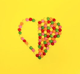 Minimal concept heart shape made of colored candies. Creative idea on yellow background. Flat lay.