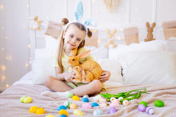 Easter, a little girl with painted colored eggs, tulips, a rabbit and bunny ears at home in a bright room is preparing for the holiday smiling and having fun