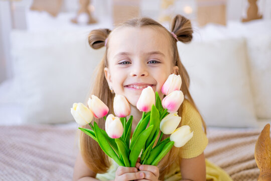 close-up portrait of a cute child with spring flowers pink tulips smiling and rejoicing or giving as a gift, women's day or mother's day