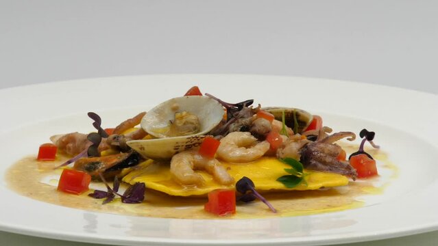 Ravioli ai Frutti di mare. Primo piatto, tradizione italiana dei ristoranti sul mare. 
Presentazione di un piatto bianco che gira, con vongole veraci, gamberi, calamaro e pomodoro. 
